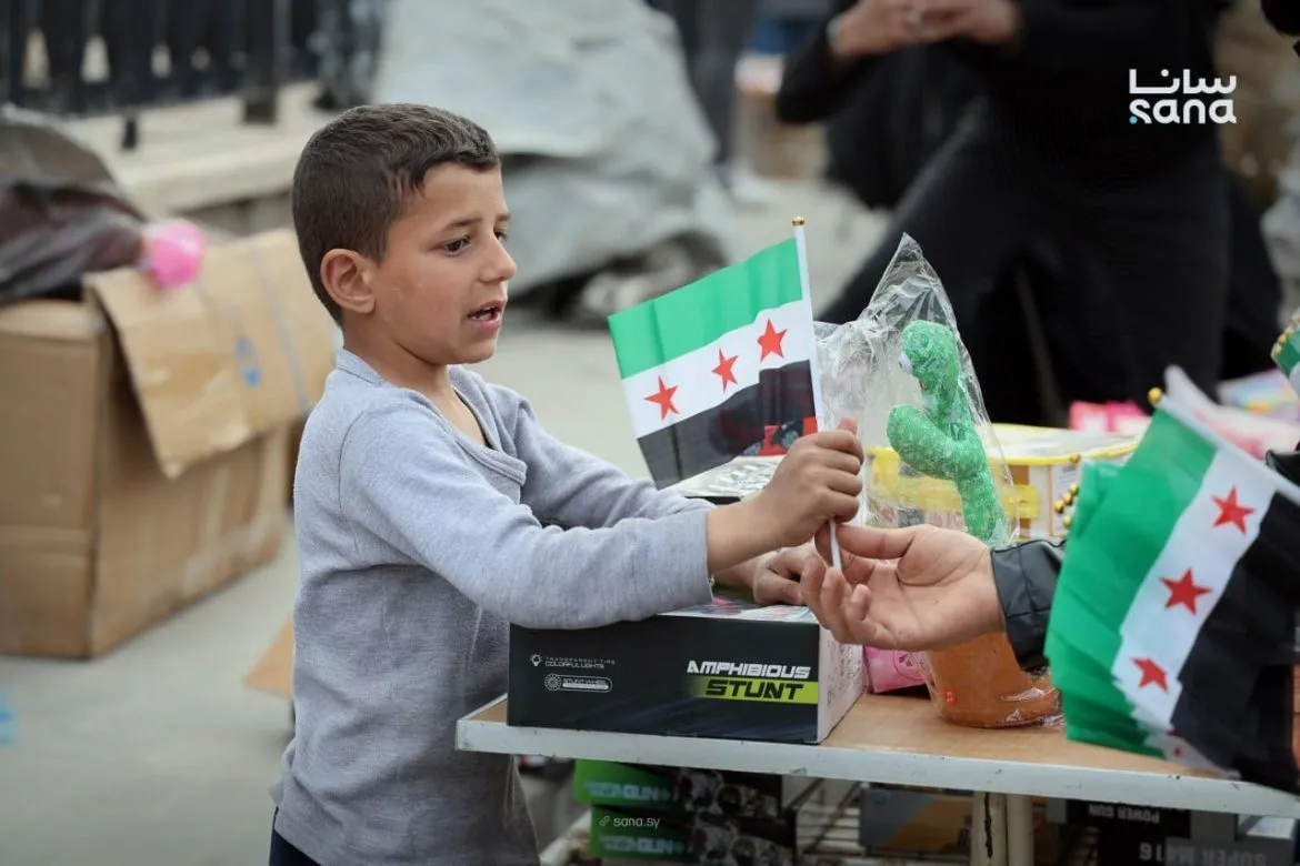 أهالي حماة يوزعوا أعلام على الأطفال بمناسبة ذكرى الثورة الـ 15